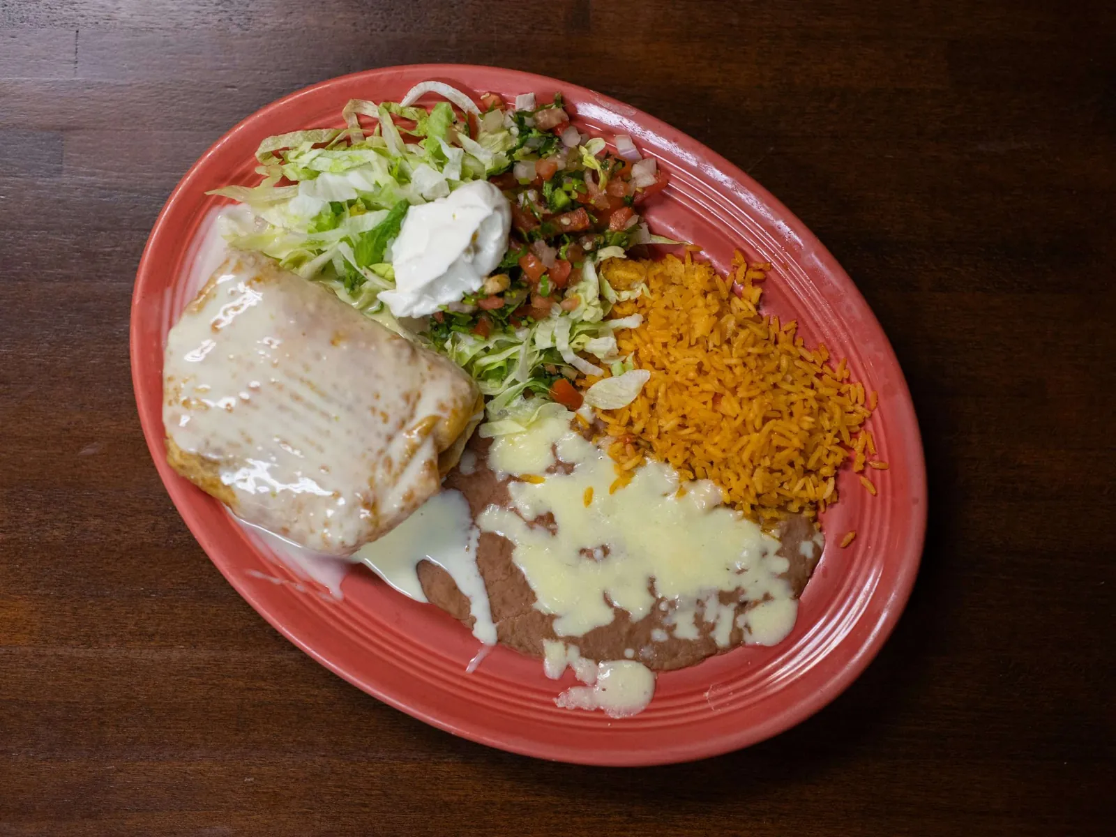 Chimichanga with cheese sauce, Mexican rice, beans and salad on a red plate